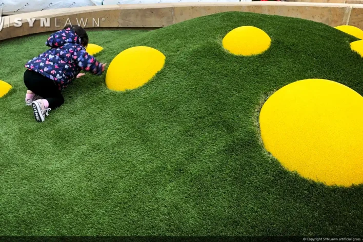 image of toddler crawling up a synthetic turf mound