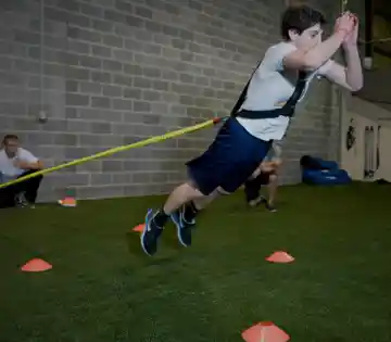 Athlete performing resisted sprint training on commercial agility turf with cone drills