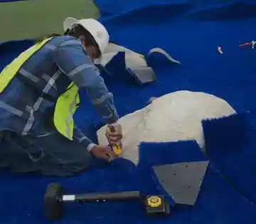 Installer trimming and fitting synthetic turf panels for a commercial golf surfacing project