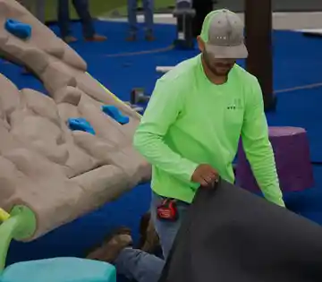 Installer fitting playground turf beneath a climbing rock wall structure