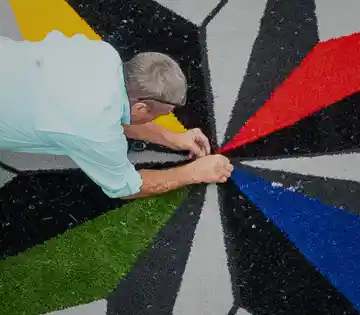 Installer hand-finishing a custom multicolor geometric turf design with seam sealing